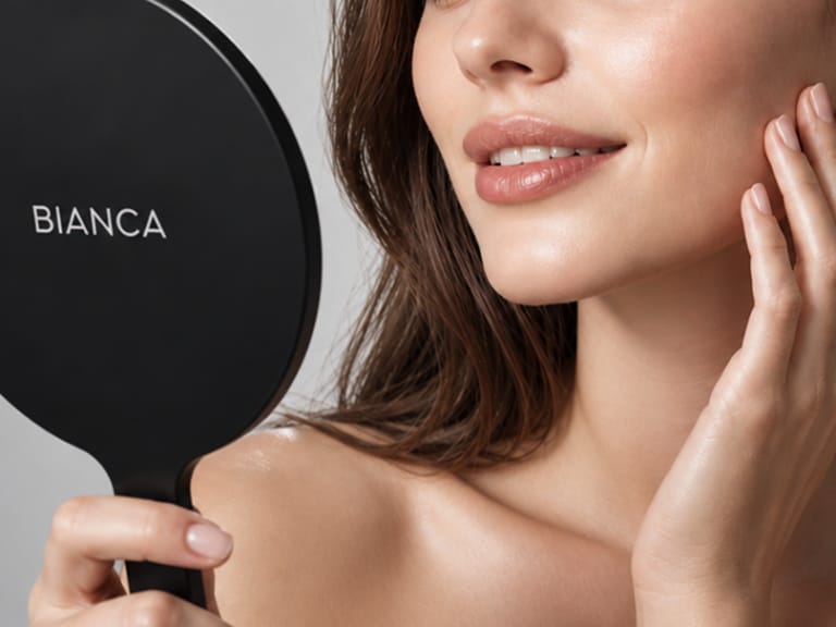 Patient smiling while holding hand mirror with BIANCA logo