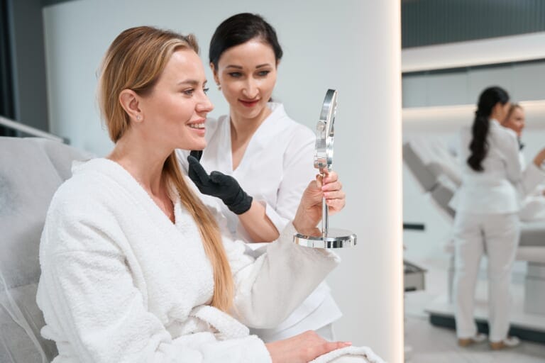 A woman viewing her results in a mirror after a cosmetic treatment.