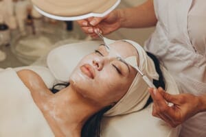 A professional applying a facial treatment to a client's skin using a cosmetic brush.