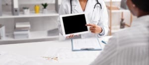 A young female doctor consulting with a patient and showing them an empty digital tablet.