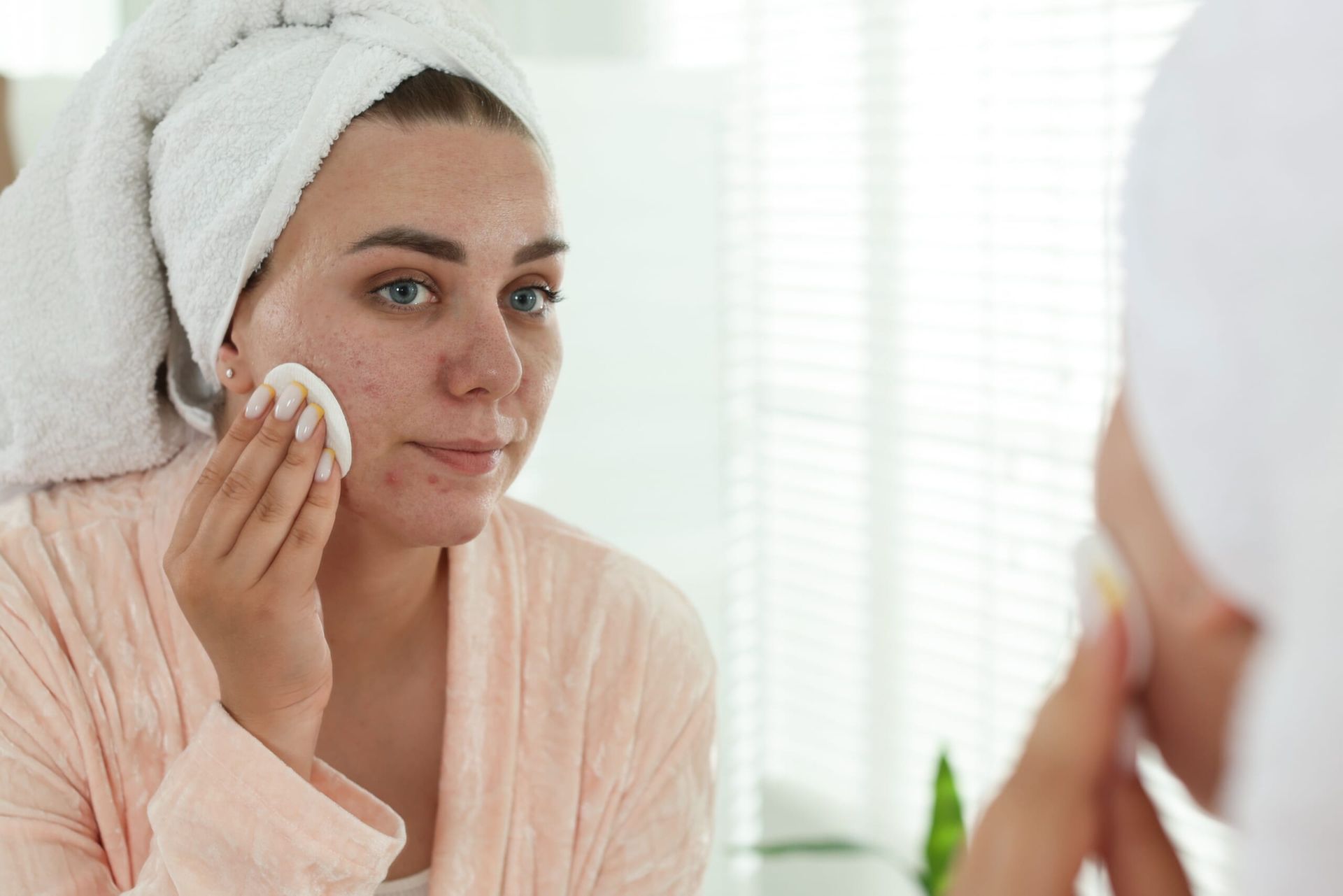 Woman covering acne with foundation in the mirror