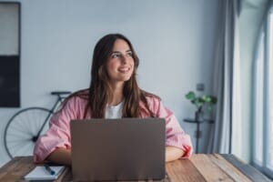 A relaxed young woman smiling at her laptop.