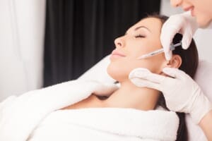 Doctor administering facial injection to a woman lying on a treatment bed