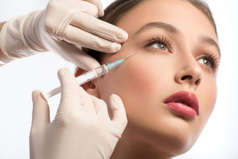 Gloved hands administering a facial injection near a woman's eye area